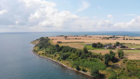 Aerial-view-paning-up-on-the-south-part-of-the-island-of-Ven-in-southern-Sweden-during-a-warm-summer-day-with-clear-water-and-fields-ready-for-harvest