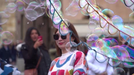 Mujer-China-De-Mediana-Edad-Con-Suéter-Brillante-Jugando-Con-Pompas-De-Jabón-En-La-Plaza-Principal-De-Praga