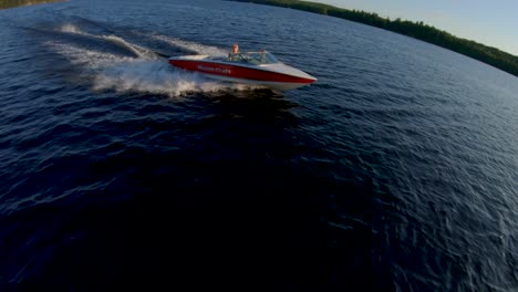 Zeitlupe---Blonde-Kaukasische-Frau-Fährt-Bei-Sommersonnenuntergang-Ein-Rotes-Und-Weißes-Wasserskiboot-Auf-Dem-Blauen-See,-Fpv-drohnenluftspur