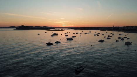 Drohnenaufnahme-Der-Küstenlinie-Mit-Booten-Im-Wasser-Mit-Sonnenuntergang-Im-Hintergrund