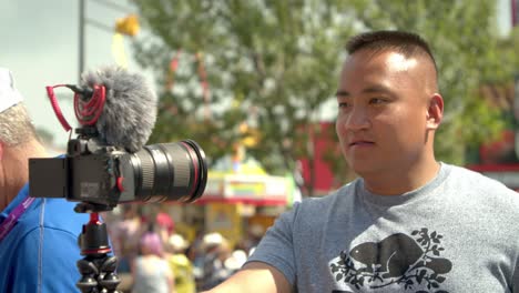 Vlogger-Asiático-Comenzando-A-Grabarse-Con-Una-Cámara-En-Una-Feria-De-Carnaval-En-Cámara-Lenta-De-4k