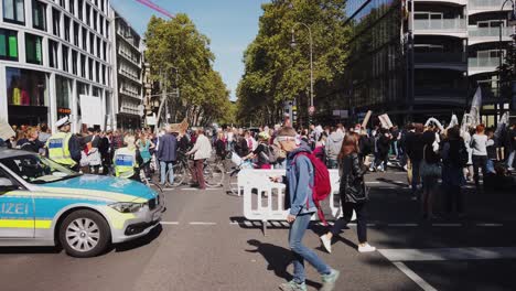 Una-Larga-Fila-De-Manifestantes-En-Una-Marcha-De-Protesta-Contra-El-Cambio-Climático-Y-Por-La-Acción-Política-Para-Detener-El-Calentamiento-Global-Está-Pasando-Por-Un-Coche-De-Policía-Que-Ha-Detenido-El-Tráfico