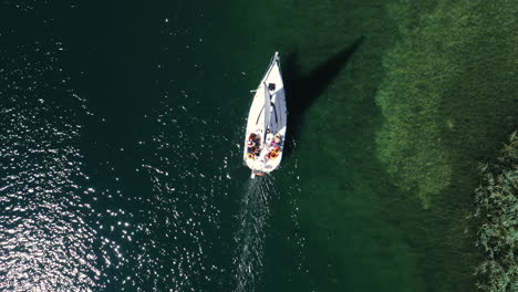 AERIAL:-Top-Down-View-of-White-Yacht-With-Group-of-People-Sailing-Near-the-Shallow-Part-of-the-Trakai-Lake
