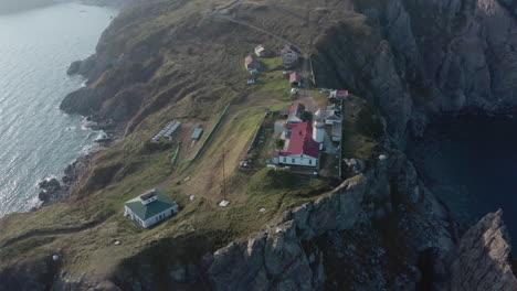 Slow-aerial-pivot-shot-of-Gamov-lighthouse-building-complex,-standing-on-steep-rocky-cliff,-on-the-sunset