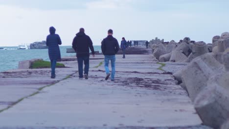 People-walking-on-Karosta-Northern-pier-in-Liepaja-in-cloudy-afternoon,-medium-shot