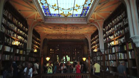 Tilt-down-from-ornate-ceiling-in-Livraria-Lello-bookstore-to-people-on-popular-staircase-in-Porto,-Portugal
