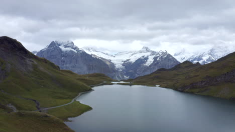 Woman-running-to-top-of-hill,-drone-fly-by-to-reveal-Lake-Bachalpsee-in-Switzerland