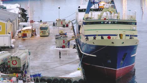 Big-transport-ship-transporting-goods-being-unloaded-by-sailors-on-the-dock-of-a-northern-coastal-city-in-Norway-Tromso