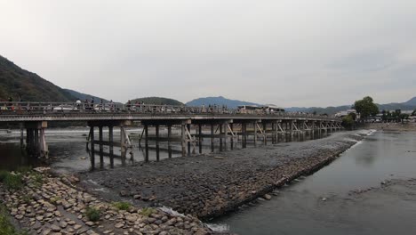 Tourists-cross-Togetsukyo-Bridge-over-peaceful-Katsura-River,-Kyoto