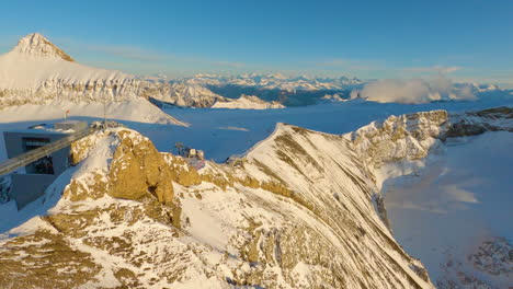 Aerial-fpv-shot-diving-towards-lookout-point-and-peak-walk-bridge,-revealing-breathtaking-swiss-alpine-winter-scene-at-sunset