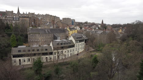 Lateral-tracking-shot-of-river-and-old-rustic-architecture-buildings-in-deal-village-in-Edinburgh,-Scotland-from-above