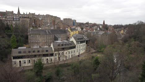 Toma-De-Seguimiento-Lateral-Del-Río-Y-Viejos-Edificios-De-Arquitectura-Rústica-En-Deal-Village-En-Edimburgo,-Escocia-Desde-Arriba