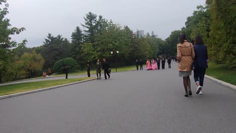 Low-angle-POV-of-someone-walking-past-groups-of-wedding-processions-in-a-park
