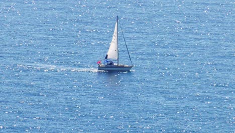 Sailing-yacht-on-wide-blue-sea-reflecting-sunlight,-slow-motion
