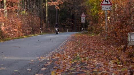 Black-clothed-biker-is-riding-on-his-motorcylce-through-the-autumn-forest