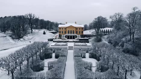 Drone-aerial-flight-over-snow-covered-garden-towards-old-Gunnebo-palace