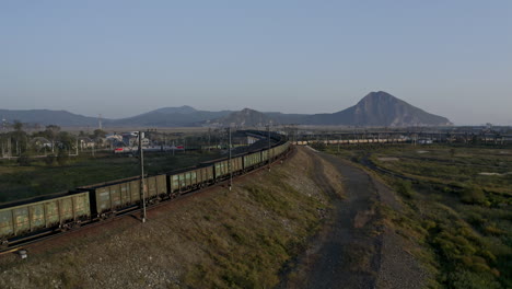 Empty-and-full-loaded-coal-cargo-train-locomotives-pulling-long-carriage-trains-on-the-intersection-of-the-railways-with-the-railway-bridge,-on-the-sunset