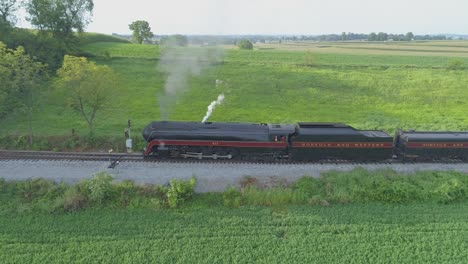 Una-Vista-Aérea-De-Un-Tren-De-Vapor-No-611-Que-Sopla-Humo-A-Través-Del-Campo-Agrícola-En-Un-Día-Soleado-De-Verano-Con-Campos-Verdes