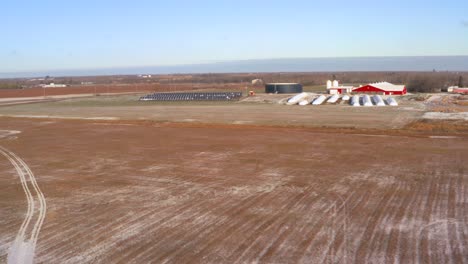 Vista-Aérea-De-Drones-De-Una-Estación-De-Paneles-Solares-Ligeramente-Cubierta-De-Nieve-Que-Alimenta-Una-Granja