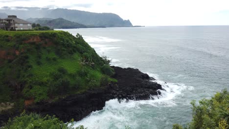 4K-Hawaii-Kauai-Short-truck-left-to-right-from-greenery-to-reveal-waves-crashing-on-rocky-shore-with-mountains-in-distance