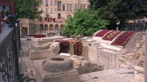Teppiche-Mit-Verschiedenen-Ornamenten-Auf-Den-Ruinen-Der-Altstadt-Von-Baku---Menschen-Stehen-Und-Beobachten