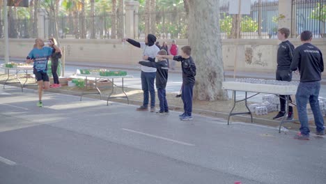 Marathon-runner-pass-the-volunteering-teens-giving-them-water-bottles,-slow-motion-from-left-to-right