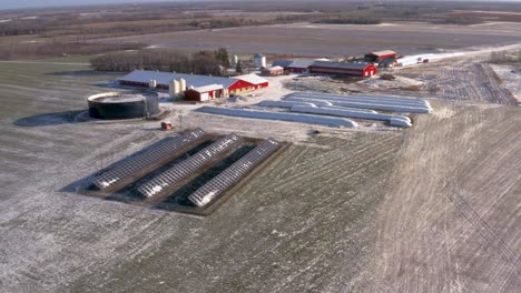 Vista-Aérea-De-Drones-De-Una-Estación-De-Paneles-Solares-Ligeramente-Cubierta-De-Nieve-Que-Alimenta-Una-Granja