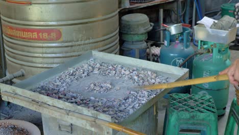 Man’s-hand-spreading-burning-coal-in-circle-shape-on-tin-dish-with-bamboo-stick