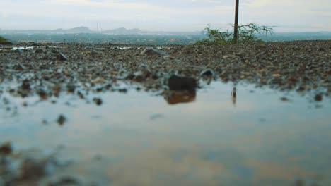 Regen-Verursacht-Pfütze-Auf-Der-Straße-Von-Curaçao-Mit-Wunderschöner-Landschaft-Im-Hintergrund---Nahaufnahme