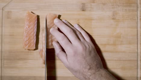 Top-down-view-of-a-hand-holding-a-piece-of-salmon-cutting-the-fresh-raw-fish-with-a-large-kitchen-knife