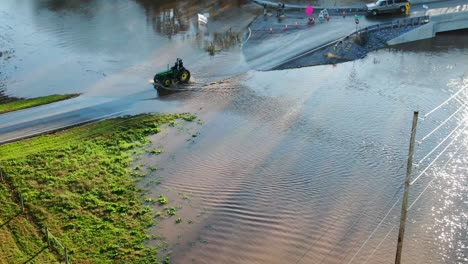 El-Tractor-John-Deere-Con-Ruedas-De-Acero-Conduce-Por-Una-Carretera-Inundada,-Vista-Aérea