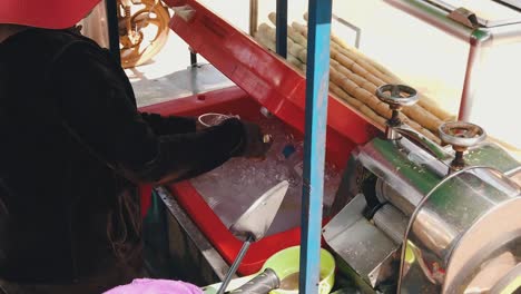 Slow-Motion-Shot-of-a-Lady-Putting-Ice-in-a-Plastic-Cup-and-Pouring-Sugar-Cane-Juice