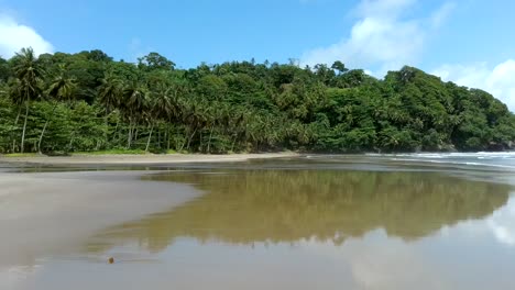 Aerial-along-empty-black-sand-beach-with-mirror-effect,-São-Tomé-Island
