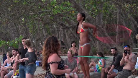 Girl-dancing-with-hoola-hoops-in-front-of-people-during-a-beach-party-near-Santa-Teresa,-Costa-Rica