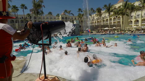 Un-Tipo-Con-Un-Sombrero-Alto-Rociando-A-La-Gente-En-Una-Fiesta-De-Espuma,-En-La-Piscina-De-Un-Resort,-En-Cabo-San-Lucas,-México