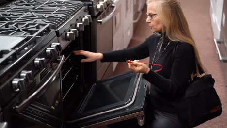 Pretty-mature-blonde-woman-looking-at-the-features-and-benefits-of-a-gas-stove-in-a-kitchen-appliance-store