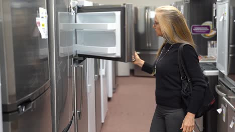 Pretty-mature-blonde-woman-shopping-for-a-refrigerator-in-a-kitchen-appliance-store