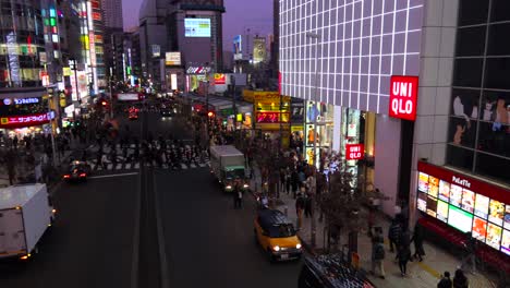 Calle-Concurrida-Con-Cielo-Púrpura-En-La-Ciudad-De-Shinjuku-Tokio,-Centro-De-La-Carretera-Con-Gente-Caminando-Y-Cruzando,-Escena-Nocturna,-4k-Paneo-A-La-Izquierda