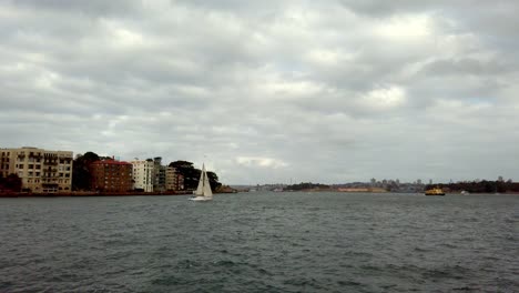 Segelboot-Am-Hafen-Mit-Wohnhäusern-Und-Wasserflugzeug-Weit-Am-Himmel-An-Einem-Bewölkten-Tag,-Stabile-Handaufnahme