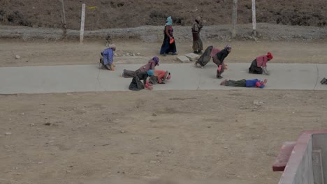 Tibetan-women-pilgrims-performing-a-ritualistic-prayer-by-walking-and-laying-on-the-ground-in-faith---Wide-pan