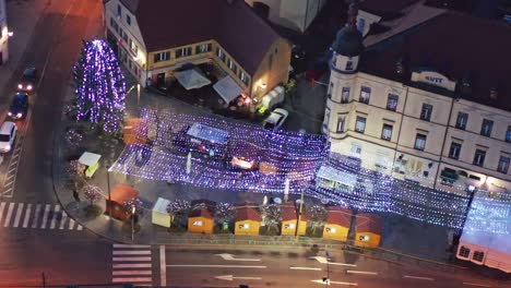 Christmas-fair-with-decoration-and-bright-lights-on-main-square-of-small-town-in-Europe,-aerial-view-of-old-medieval-town-center