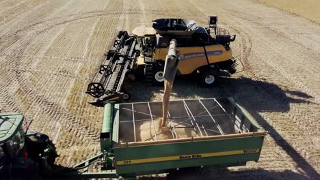 A-combine-unloads-freshly-harvested-corn-into-a-tractor-trailer---orbiting-aerial-view
