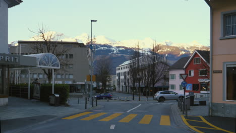 Vaduz-Liechtenstein,-Coches-Dando-La-Vuelta-A-Una-Rotonda-Con-Montañas-Nevadas-Visibles-En-El-Fondo