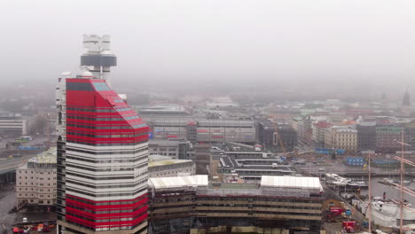 Aerial-push-in-towards-The-Lipstick-building-in-Gothenburg,-hazy-sky