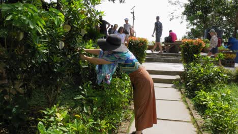 A-woman-in-colorful-clothes-puts-a-leaf-hanger-on-a-tree-near-Big-Buddha,-Phuket