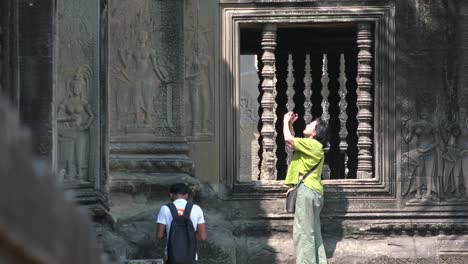 Plano-Medio-De-Una-Turista-Tomando-Fotos-Fuera-De-Las-Hermosas-Tallas-De-Las-Paredes-Mientras-Un-Niño-Nos-Da-La-Espalda-En-La-Esquina