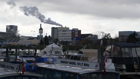 Medium-shot,-boat-and-ferry-park-in-the-Rhine-river,-smoke-coming-out-of-a-chimney-in-the-background