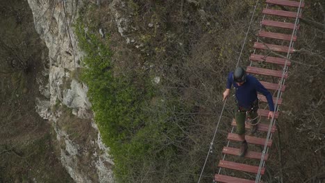 A-tourist-experiencing-a-walk-on-the-wooden-hanging-bridge-in-Via-ferrata,-located-in-the-Alps---tilt-down