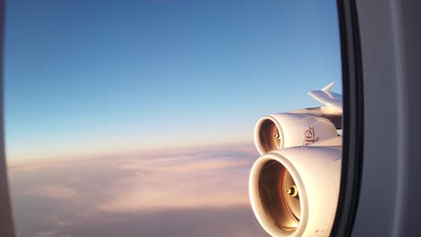 View-out-window-of-huge-airplane-with-morning-sunlight-glowing-on-massive-engines-and-purple-hue-on-clouds-with-blue-sky-above