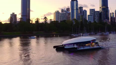 Lugar-De-Entretenimiento-De-Yates-De-Lujo-Que-Pasa-Por-El-Agua-Serena-Con-Torres-Modernas-Y-Edificios-Urbanos-Durante-La-Puesta-Del-Sol-En-Brisbane,-Australia